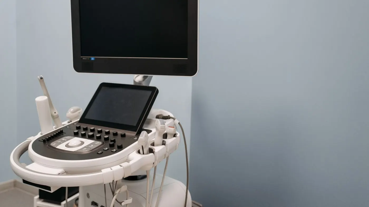 Equipo de ecografía con pantalla y teclado en un consultorio de paredes azules: imagen para la guía del ecocardiograma